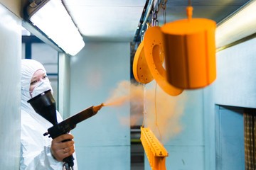 Powder coating of metal parts. A woman in a protective suit sprays powder paint from a gun on metal products - obrazy, fototapety, plakaty