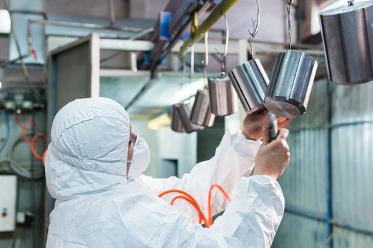woman in protective suit blows air on the metal parts before powder painting