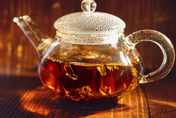 Прозрачный стеклянный чайник с черным чаем на коричневом фоне