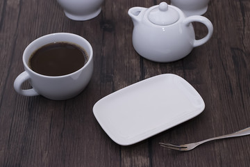 Fototapeta na wymiar A white cup of coffee and other white utensils on brown wooden table. Breakfast.