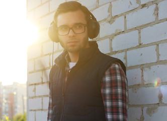 Portrait of a handsome young man with headphones. A man with a beard listens to his favorite music in large professional headphones on the street.