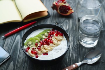 Day planning, time management, healthy food and lifestyle concept. Delicious oatmeal and yoghurt smoothie bowl with fruit slices and pomegranate seeds for breakfast on table with paper planner.