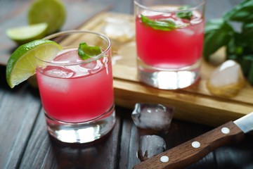 Refreshing iced strawberry cocktail with lime slices and basil on wooden board with melting ice cubes. Summer beverages, bar concept