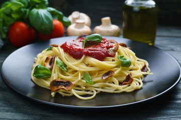 Prepared spaghetti pasta with tomato sauce, roasted champignons and basil leaves on black plate. Italian cuisine food background concept