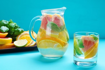 Refreshing healthy homemade citrus lemonade served in glass pitcher with fruit slices and basil on blue background, cold delicious summer drink
