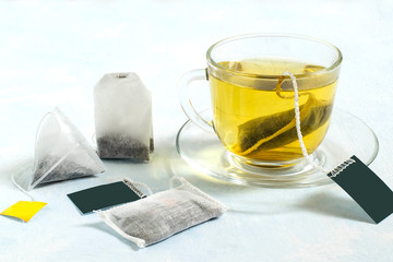 Several tea bags and cup of tea on light blue background
