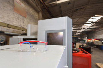 Protective transparent glasses lie on a gray surface against the background of the factory production