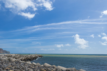 Water landscape with a striped lighthouse at the end of the pier stuck in the ocean under the blue...