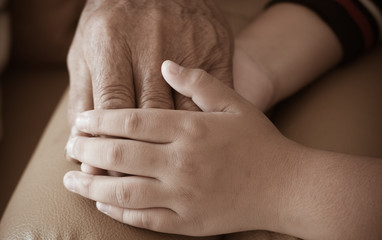 Hands of little Asian kids holding poor elderly grandfather man hands wrinkled skin with feeling care and Love. World Kindness Day concept and Adult day care center, Family Older people concept