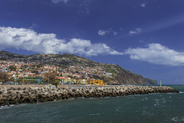 Fototapeta premium Skyline of Funchal with colorful houses on the hills, beach ath the Atlantic Ocean under the blue sky with fancy white clouds. Vacation on the eternal spring island Madeira