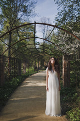 Lovely brunette girl in white romantic dress with long hair in a blooming spring garden. In the...