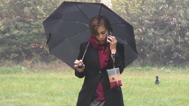 Girl talking on the phone in a park, holding an umbrella.