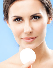 Young woman cleaning skin by cotton pad, over blue