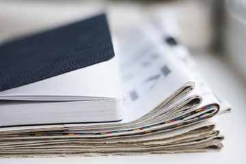 Folded newspapers and business notebook. Pile of daily papers with partially shown headlines and book for notes with leather cover. Financial journals on the desk at office, side view