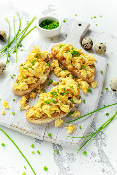 Homemade Quail Scrambled eggs on crispy toast, bread with green onion, chives on white board.