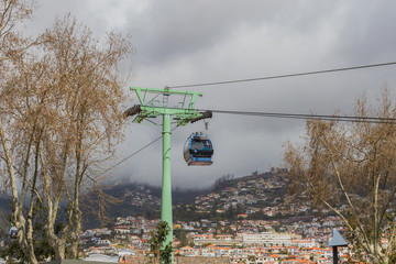 Blue color cable car wagons over the town under the cloudy sky on a foggy day