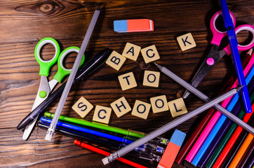 Set of the different school stationeries. Pens,  scissors, pensils, eraser on wooden desk. Back to school inscription. Top view