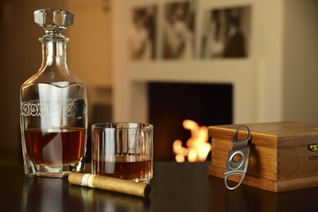 liqueur and cigar in the foreground on table and lit fireplace in the background