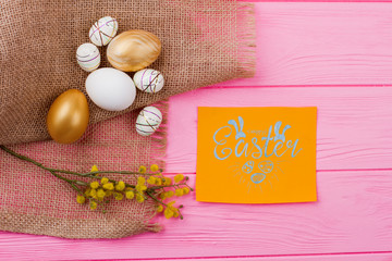 Happy Easter background with decoration. Decorative styrofoam and golden eggs with pussy-willow twig on burlap. Easter greeting card on pink wooden background.