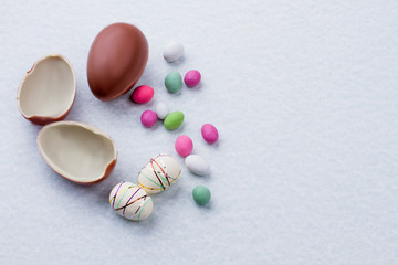 Chocolate eggs and colorful candies. Styrofoam Easter eggs on light background with copy space. Easter simple decor.