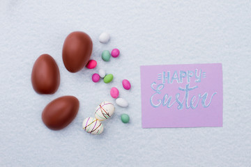 Happy Easter composition with chocolate eggs. Sweets and festive polystyrene eggs on light background. Spring season holiday.