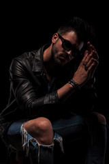 Obraz premium seated fashion man with sunglasses holding palms together