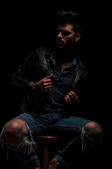 Obraz na płótnie Canvas fashion man sitting looks to side while holding jacket collar
