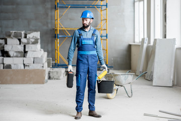 Builder in working uniform with protective helmet standing with instruments at the construction...