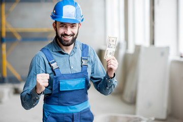 Portrait of a happy builder standing with his salary at the construction site indoors