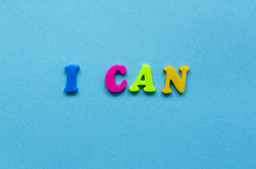 phrase "i can" of colored plastic magnetic letters on blue paper background