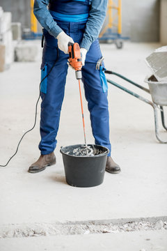 Builder in uniform mixing plaster with drill at the construction site indoors