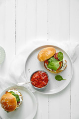 Burgers with grilled beef patties, cream cheese and spinach on classical bun. White wooden background