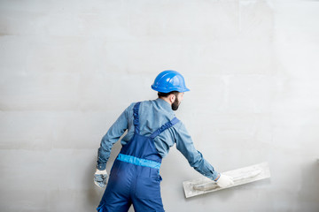 Plasterer in blue working uniform plastering the wall indoors