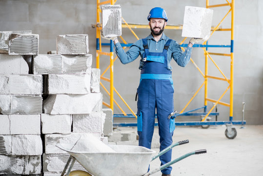 Portrait of a strong builder in uniform holding blocks at the construction site indoors