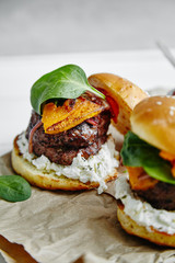Burgers with grilled beef patties, cream cheese and spinach on classical bun. White wooden background