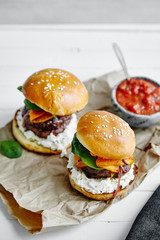 Burgers with grilled beef patties, cream cheese and spinach on classical bun. White wooden background