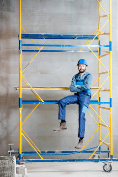Builder in blue working uniform sitting on the scaffolding indoors