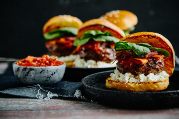Burgers with grilled beef patties, cream cheese and spinach on classical bun. Dark rustic wooden background