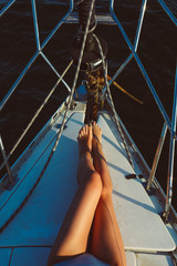 female tanned long legs on the deck of yacht in blue sea