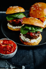 Burgers with grilled beef patties, cream cheese and spinach on classical bun. Dark rustic wooden background