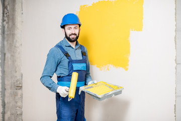 Portrait of a handsome painter in working uniform painting wall with yellow paint
