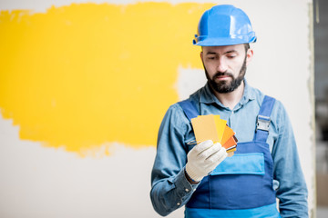 Painter in blue workwear holding color swatches on the yellow wall background indoors