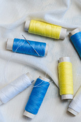 Fototapeta na wymiar Spools of blue, yellow and white threads and sewing needle on white cotton cloth