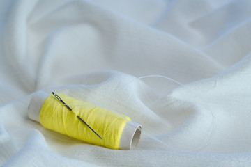 Fototapeta na wymiar Yellow thread spooll with sewing needle on white cotton cloth
