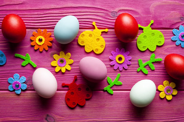 Colored Easter eggs and decorations on pink wooden background