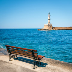 empty bench in the harbor with lighthouse in the background, Crete, Chania