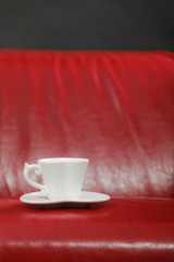 Fototapeta na wymiar Small white tea of coffee cup on red sofa