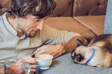 Portrait of handsome young man playing with cat and drinks coffee