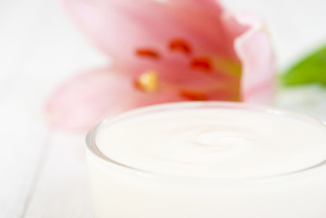 Cosmetic cream and lily flower on white wooden table