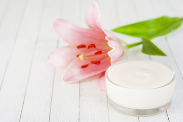 Cosmetic cream and lily flower on white wooden table